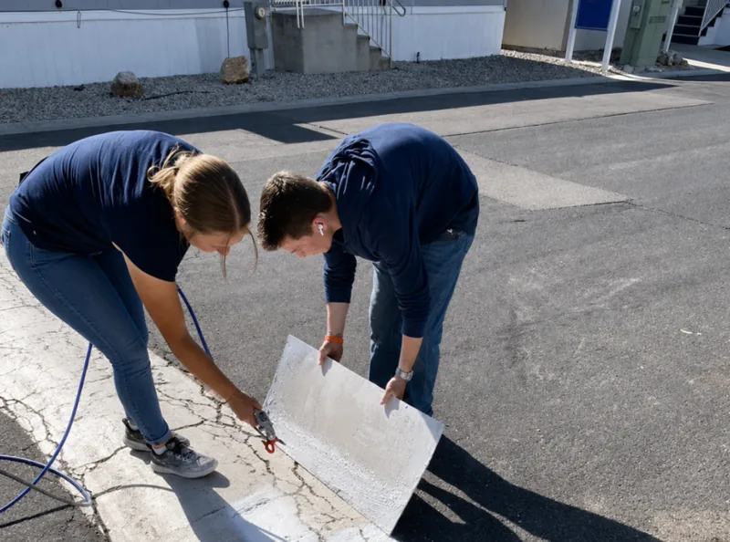 Two people working on a light-colored panel outdoors in a photo shared by LC Property Solutions.